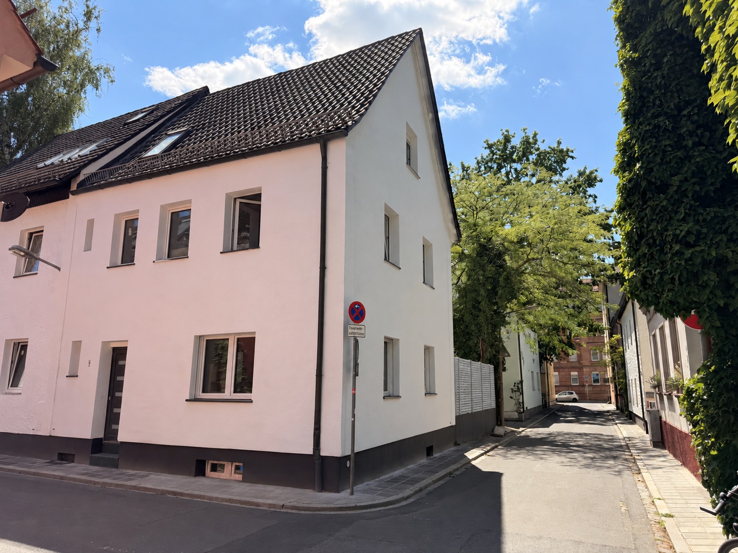 Straßenansicht mit heller Fassade, schwarzer Eingangstreppe und grauem Gartenzaun